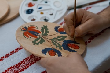 handpainting on handmade decorative wooden round plate, man's hand paints a bright floral pattern with a brush, Petrykivka painting style, finishing touch