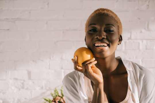 cheerful african american woman with short hair holding orange