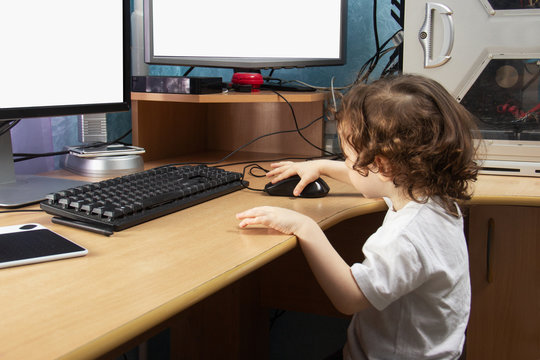 Little 2 3 year old baby girl in white clothers draws at the home computer in graphics drawing tablet. two monitors. The child is holding a mouse. Mock up vith copy space for text