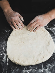 men's hands knead a round piece of dough for making pizza