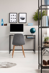 Grey chair at desk with computer and globe in fashionable workspace in modern home interior