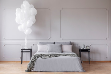 Front view of a double bed with pillows next to balloons in a grey bedroom interior