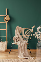 Wicker armchair with beige blanket and wooden ladder with wicker hat, real photo with copy space on...