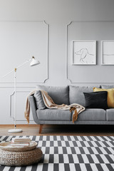 Real photo of a grey sofa, striped rug and pouf in a living room interior