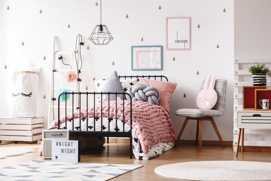 Cozy pastel pink woolen blanket on single industrial bed in scandinavian bedroom interior for teenager, grey raindrops and posters in frames on the wall