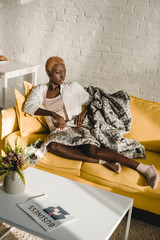 confident african american woman lying on yellow sofa in living room