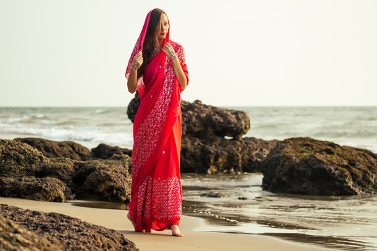 Young women wearing a red saree on the beach goa India.girl in traditional indian sari on the shore of a paradise island among the rocks and sand enjoying the freedom and the sunset