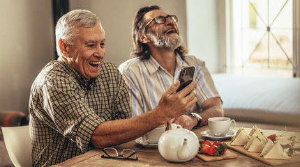 Retired men looking at old photographs on smartphone and laughin