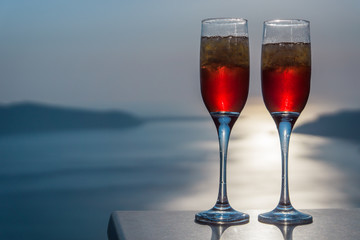 Two red champagne style coctail drinks overlooking the sunset and the sea in Santorini/Greece.