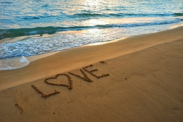 Valentines day concept, love heart shape handwriting on sand beach in sunrise and blue ocean.
