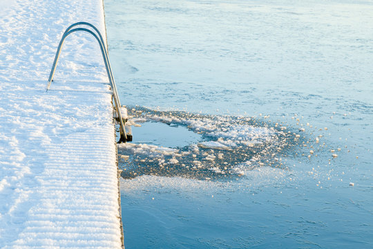 Ladder at lake footbridge. Fresh ice hole for swimming. Cold day. Care about body health in winter time. Side view.