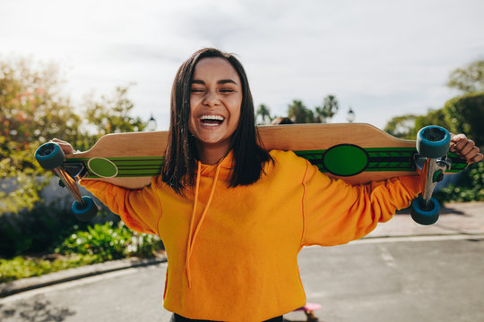Girl standing in street with a longboard - Powered by Adobe