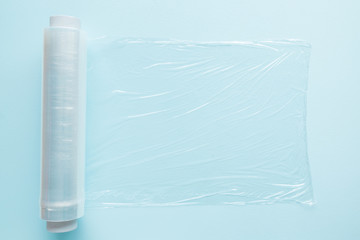 Roll of transparent polyethylene food film for packing products on the pastel blue table. Empty place for text or objects. Top view.