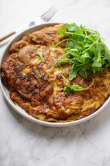Tortilla omelette with sliced potatoes and herbs on marble table