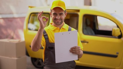 Happy delivery man holds a clipboard and shows ok