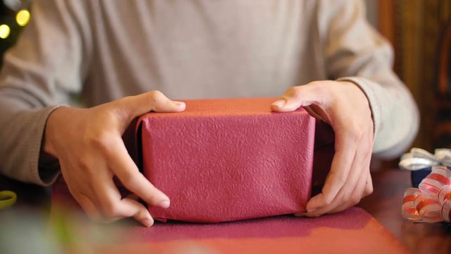 Close-up view of unrecognizable man sitting at table and wrapping Christmas present for girlfriend with pink paper