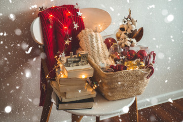 Winter sweater laid on a chair with a basket of Christmas decorations, books. Holiday decoration with the inscription HOME. 