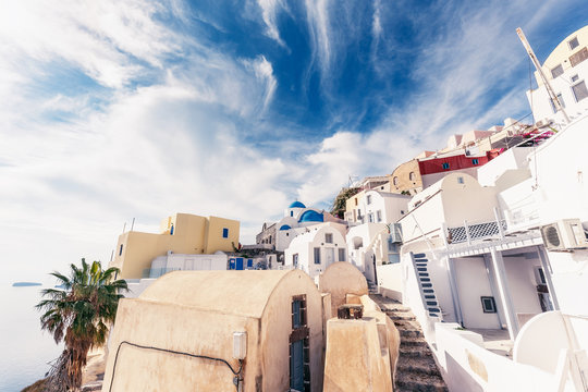 Famous churches in Oia village, Santorini island in Greece, on a sunny day with dramatic sky. Scenic travel background.