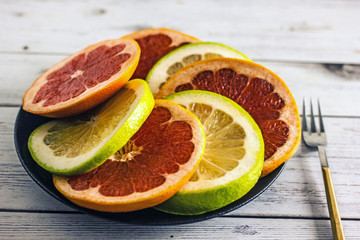 Rings of grapefruit and pomelo on a plate of different colors, next to a fork. Background with citrus. Background with grapefruit