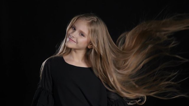 Portrait of little model in studio isolated on black background. Touching her hair in slow motion, looking at camera, posing. hd
