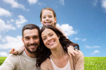 family and people concept - happy mother, father and little daughter over blue sky and grass background
