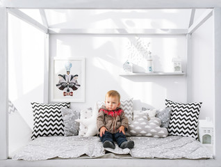 Serious little boy sitting on a bed with a set of pillows.