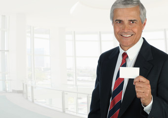 Mature businessman in high key office setting holding a blank business card