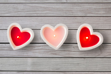 valentines day and decoration concept - heart shaped candles burning over grey wooden boards background