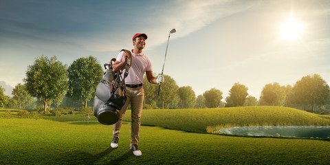 Male golf player on professional golf course. Smiling golfer walking on fairway with golf bag and...