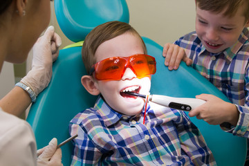 Reception at the dentistry. A little boy lays on the couch and his brother puts the lamp in his mouth