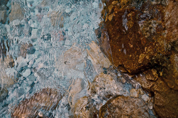 Beautiful multi-colored stones playing colors in a raging stream of river water. Abstract modern and stylish background for design or print