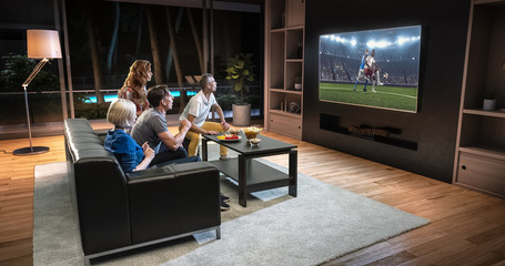 Fototapeta premium Group of students are watching a soccer moment on the TV and celebrating a goal, sitting on the couch in the living room.