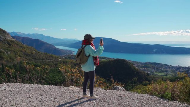 A woman takes a picture of the landscape on the phone while standing on top of a mountain. Slow motion