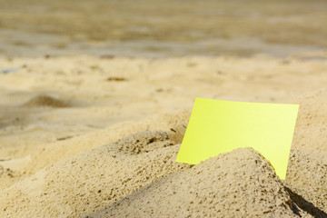 A blank yellow card buried in sand at the beach
