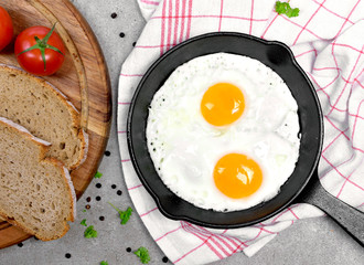 Delicious fried eggs in a cast iron pan. Top view of eggs and bread, breakfast scene.