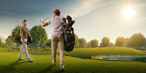Two male golf players on professional golf course. Smiling golfers walking with golf clubs and golf...