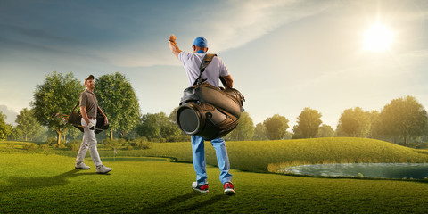 Two male golf players on professional golf course. Smiling golfers walking with golf clubs and golf...