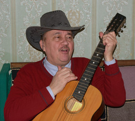 Man in cowboy hat is playing the guitar and singing.