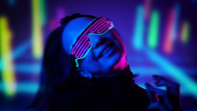 Paortrait young girl in glowing glasses dancing and moving her head to the music in neon lights. Enjoying dance music concept.