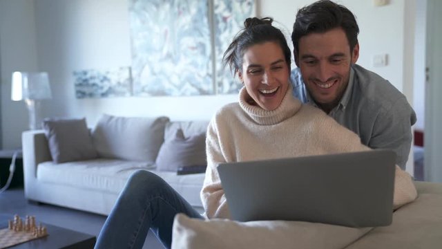 Attractive relaxed couple sharing laptop in modern home 