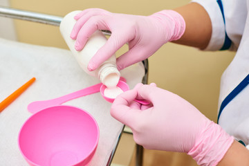 hands of a doctor pour white liquid into a pink container