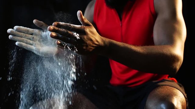 african american sportsman covering hands with talc powder before training at gym in slow motion