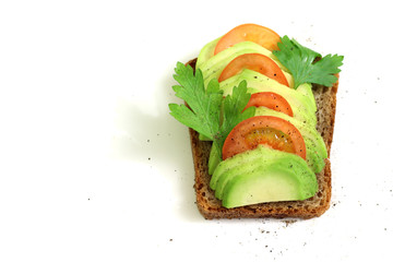 Avocado sandwich with tomato and seasoning on dark rye bread.