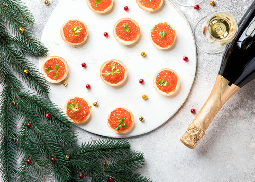 Christmas and New Year holidays composition. Red Salmon Caviar in Tartlets. Festive Appetizer and champagne on  gray background.Copy space for Text.