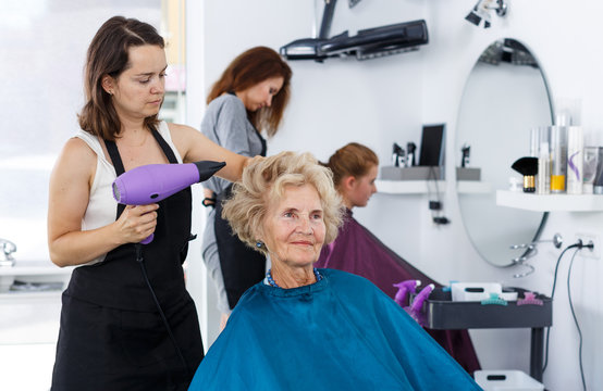 Hairdresser drying hair of elderly female
