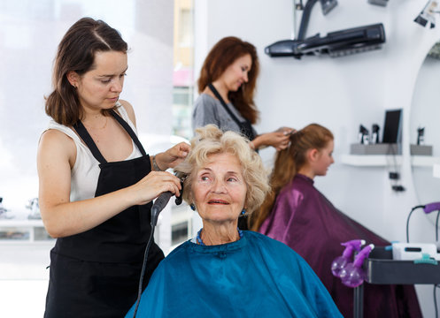 Hairdresser curling hair of elderly female