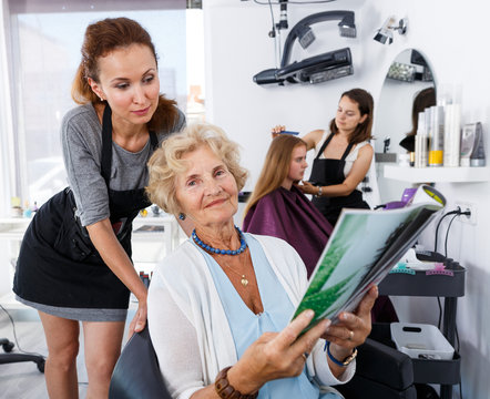 Hairdresser with senior woman choosing hairstyling in magazine