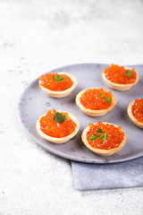 Holidays composition. Red Salmon Caviar in tartlet on a plate. Festive Appetizer  on  gray background.Copy space for Text.