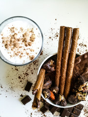 Chocolate bars, chocolates, chocolate tubes sprinkled with cocoa in a white bowl with a glass of milk next.