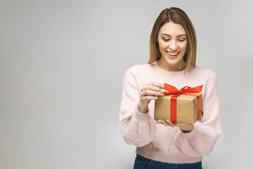 Image of Happy brunette woman in casual holding gift box and looking at the camera isolated over...